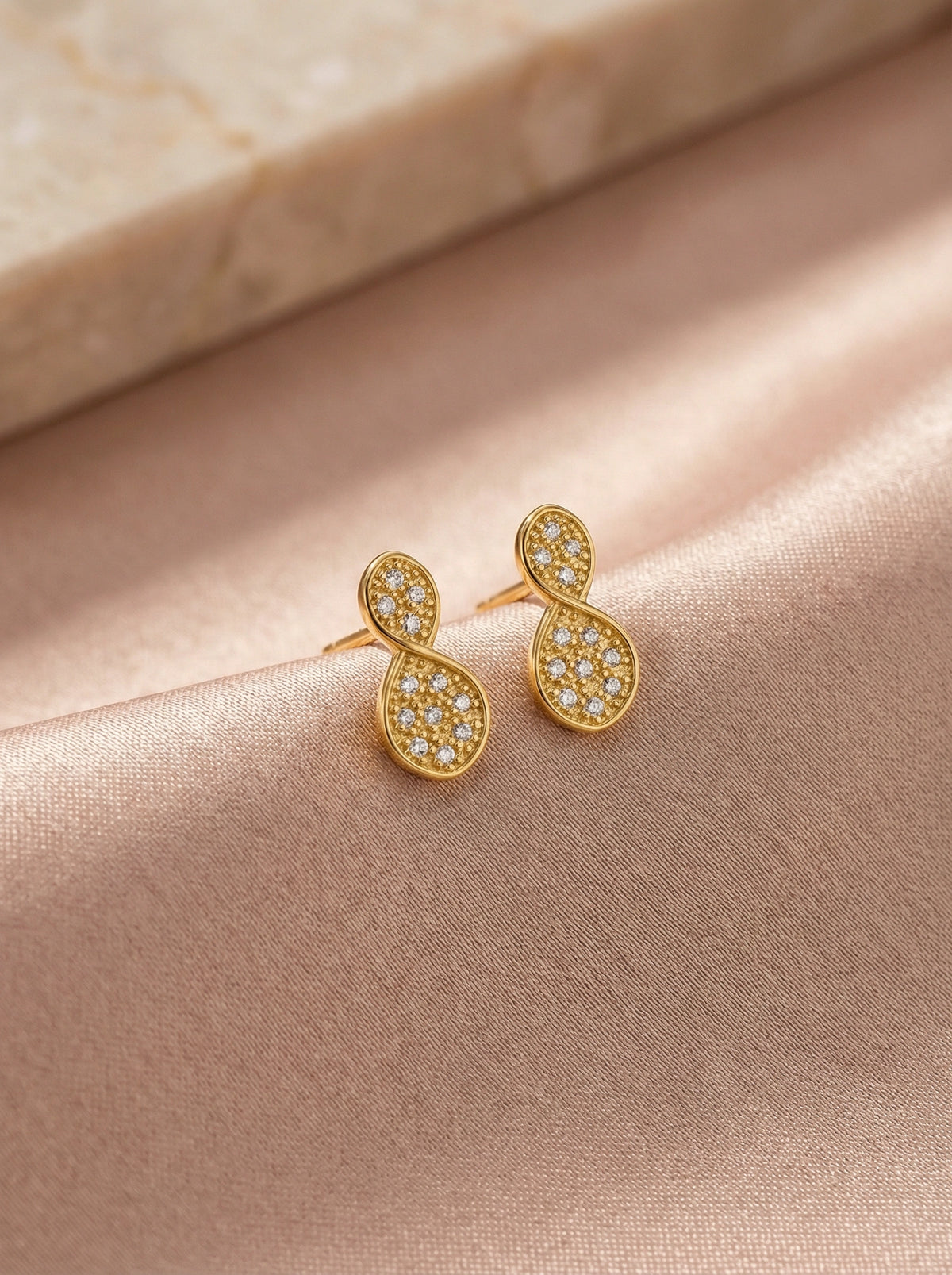 18k Gold plated earrings with diamond accents on a soft pink fabric background