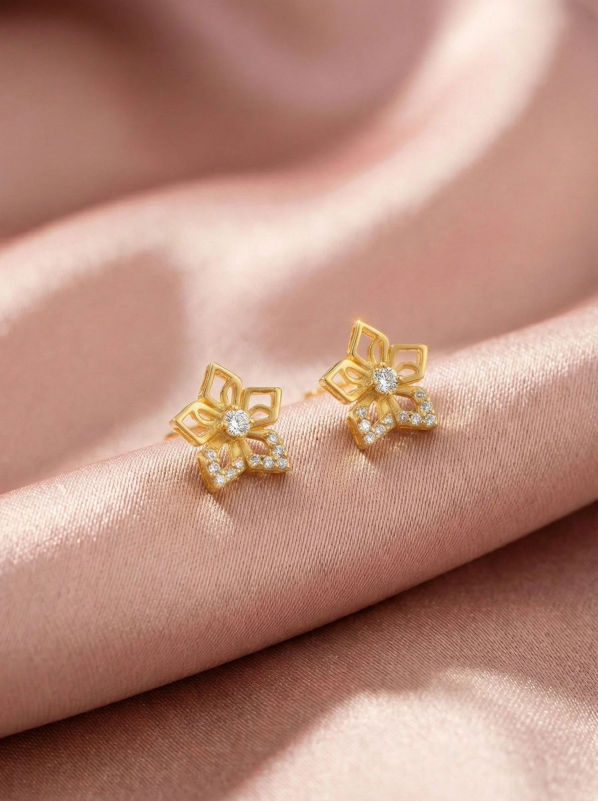 18k gold plated flower-shaped earrings with clear stones on a pink fabric background