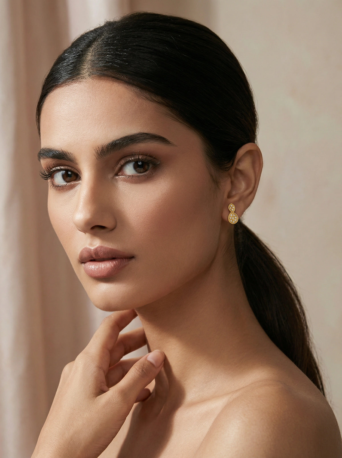 woman with a ponytail wearing 18k  gold plated earrings against a beige background