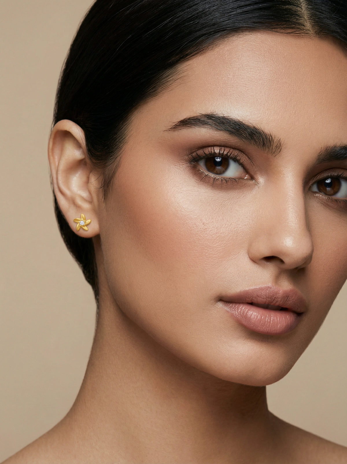 close-up of a woman wearing a 18k gold plated earring against a beige background