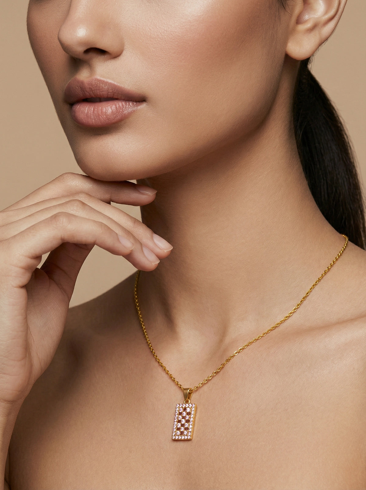 close-up of a woman wearing a 18k gold plated necklace with a diamond pendant against a beige background