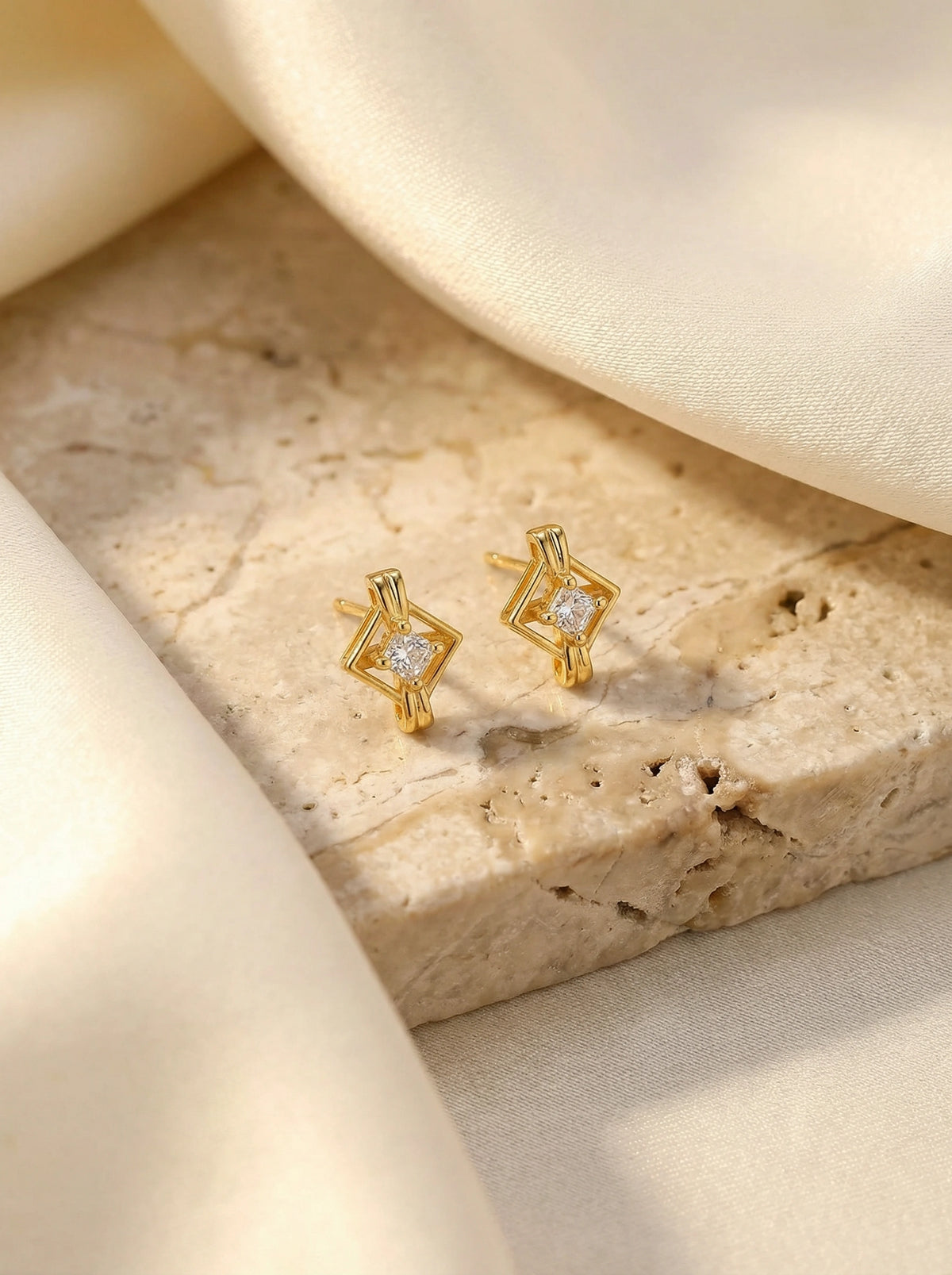 18k gold plated earrings with diamond-like stones on a textured beige surface