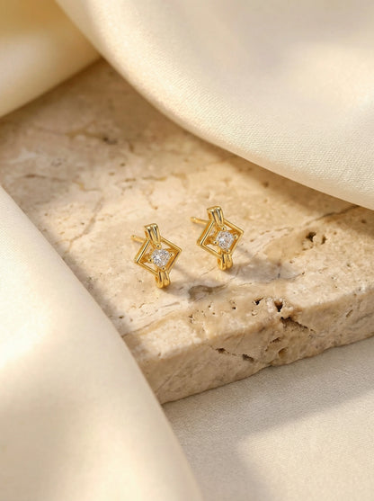 18k Gold plated earrings with diamond-like stones on a textured beige surface