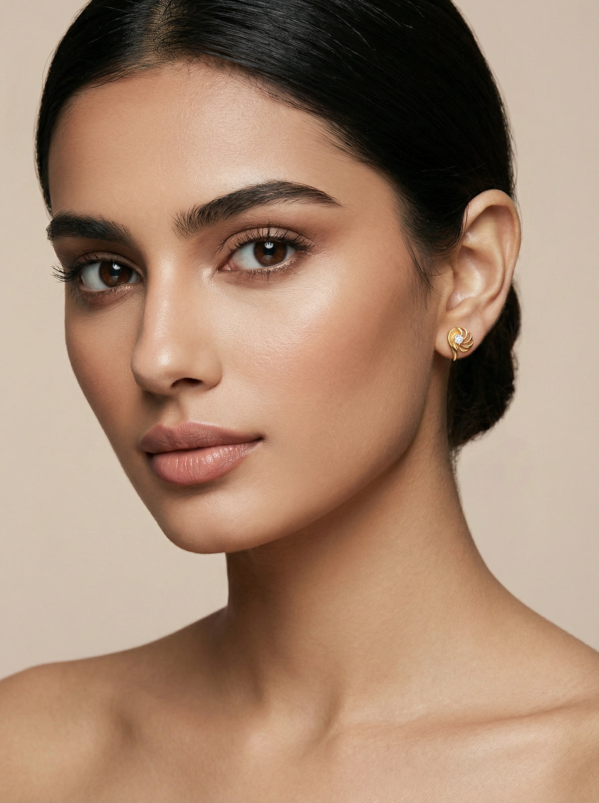 close-up of a woman wearing 18k gold plated earrings against a beige background