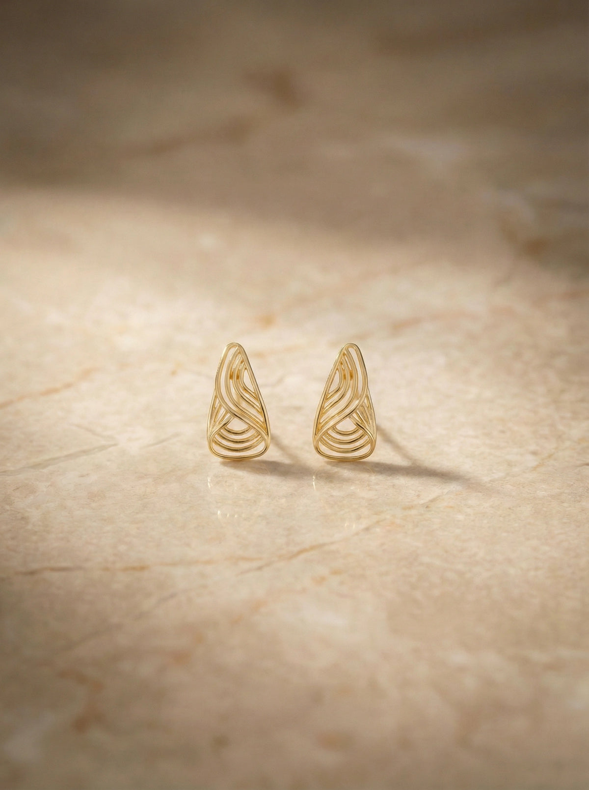 18k gold plated wing-shaped earrings on a beige surface